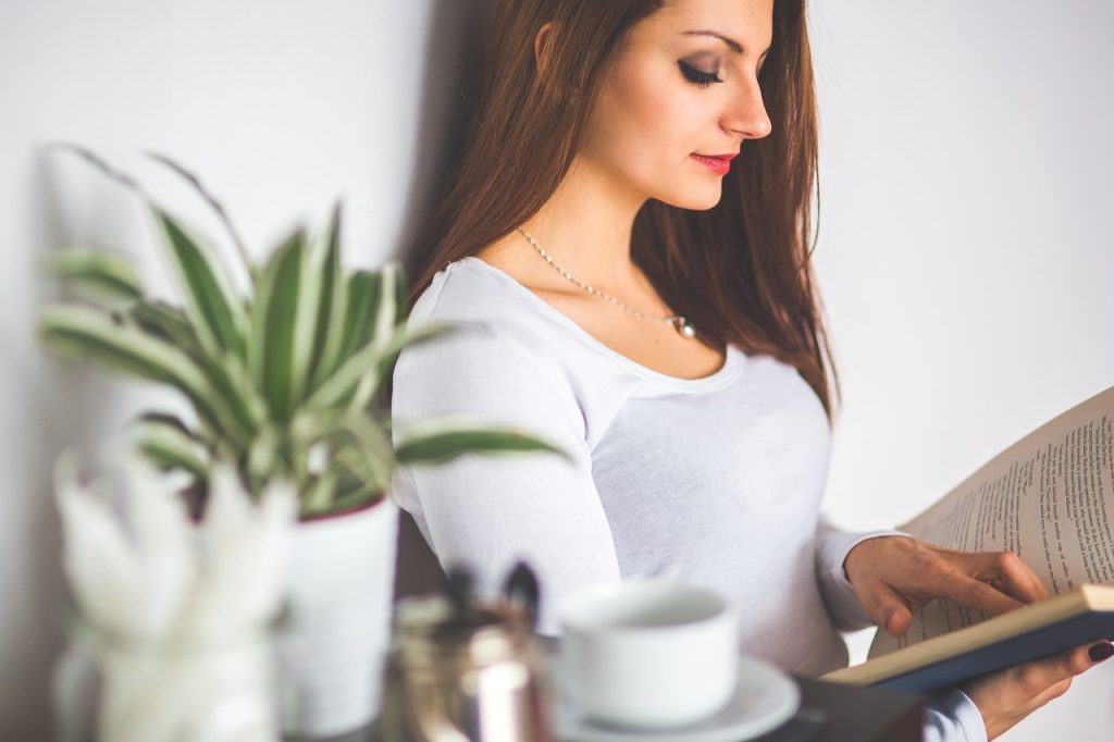 A woman reads a book while enjoying a cup of tea, creating a peaceful moment of self-care and relaxation.