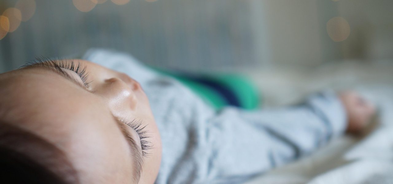 Toddler resting on a bed, unwell and tired - capturing the reality of sick day survival for moms.