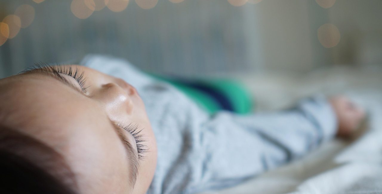 Toddler resting on a bed, unwell and tired - capturing the reality of sick day survival for moms.