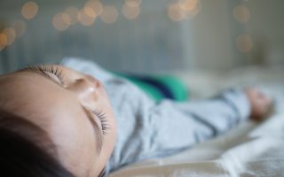 Toddler resting on a bed, unwell and tired - capturing the reality of sick day survival for moms.