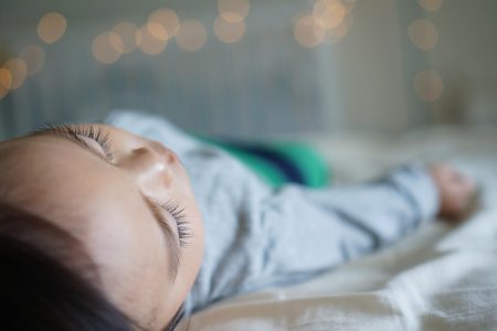 Toddler resting on a bed, unwell and tired - capturing the reality of sick day survival for moms.